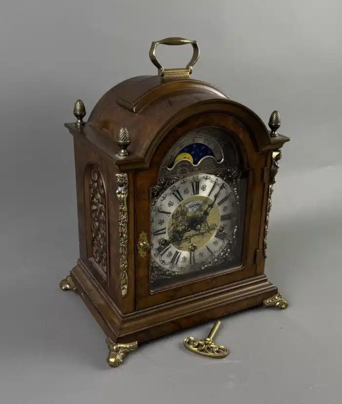 Kommodenuhr John Warmink im Barockstil Zifferblatt mit Mondphasenanzeige, römische Ziffern, braun mattiertes Holzgehäuse mit Gelbmetallapplikationen, Höhe ca. 39 cm, 1 Schlüssel, – Bild 2