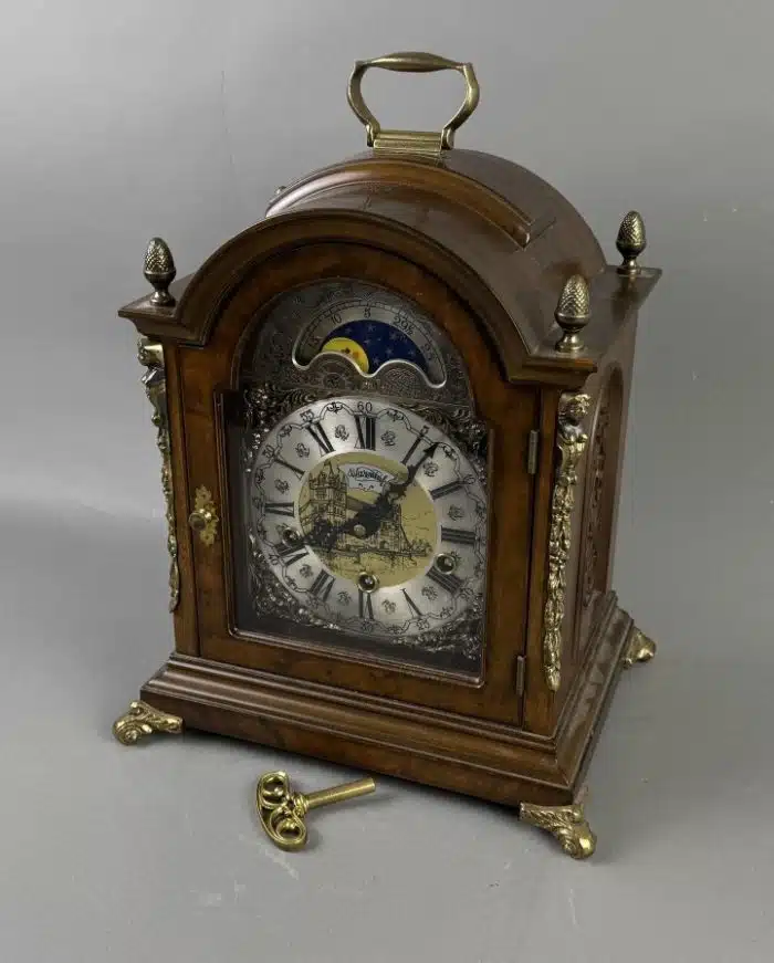 Kommodenuhr John Warmink im Barockstil Zifferblatt mit Mondphasenanzeige, römische Ziffern, braun mattiertes Holzgehäuse mit Gelbmetallapplikationen, Höhe ca. 39 cm, 1 Schlüssel, – Bild 3